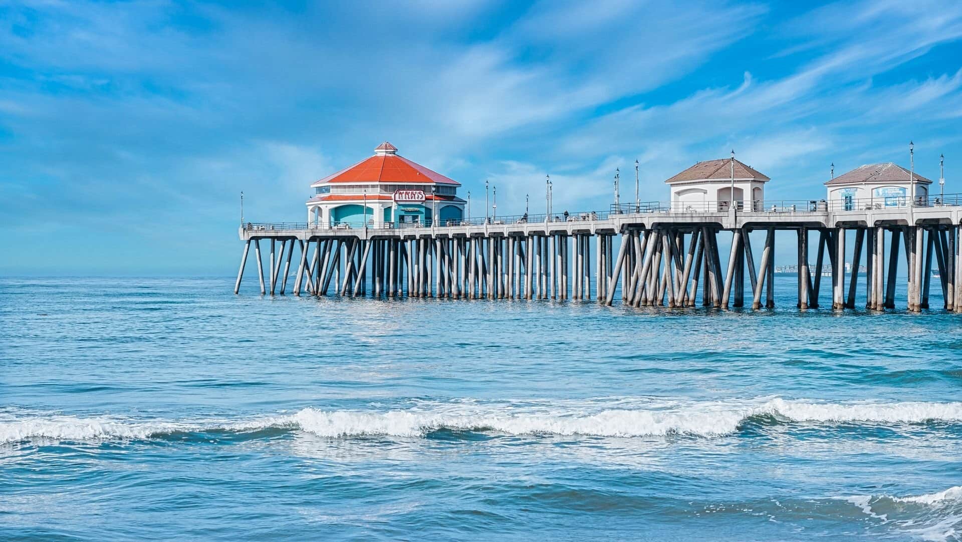 Huntington Beach Pier stretching over blue ocean waves under a bright sky in Huntington Beach, California