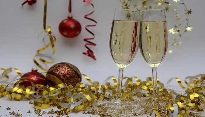 Two champagne glasses beside red ornaments and gold ribbon