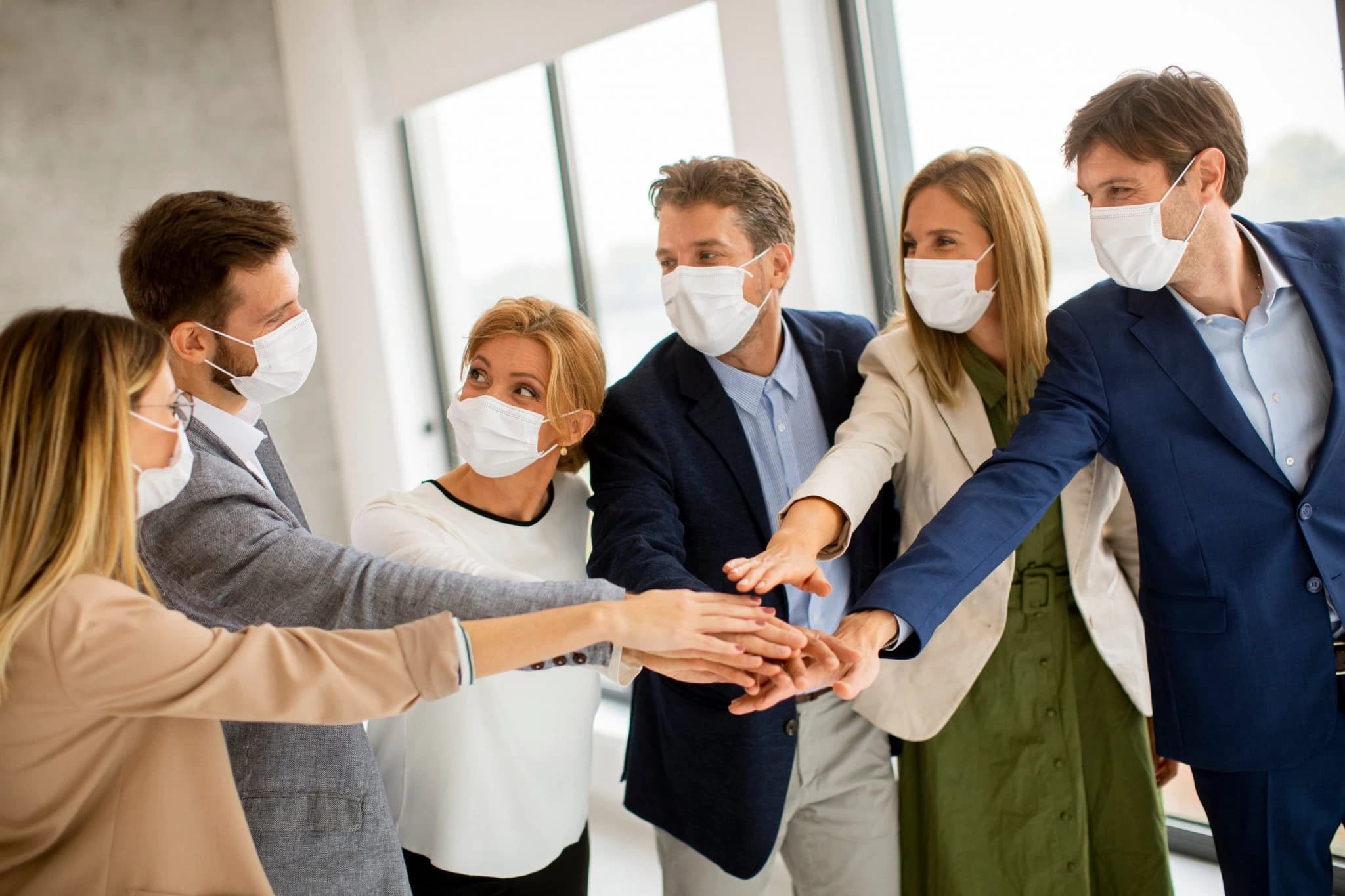 Colleagues in face masks stacking hands together in a team huddle