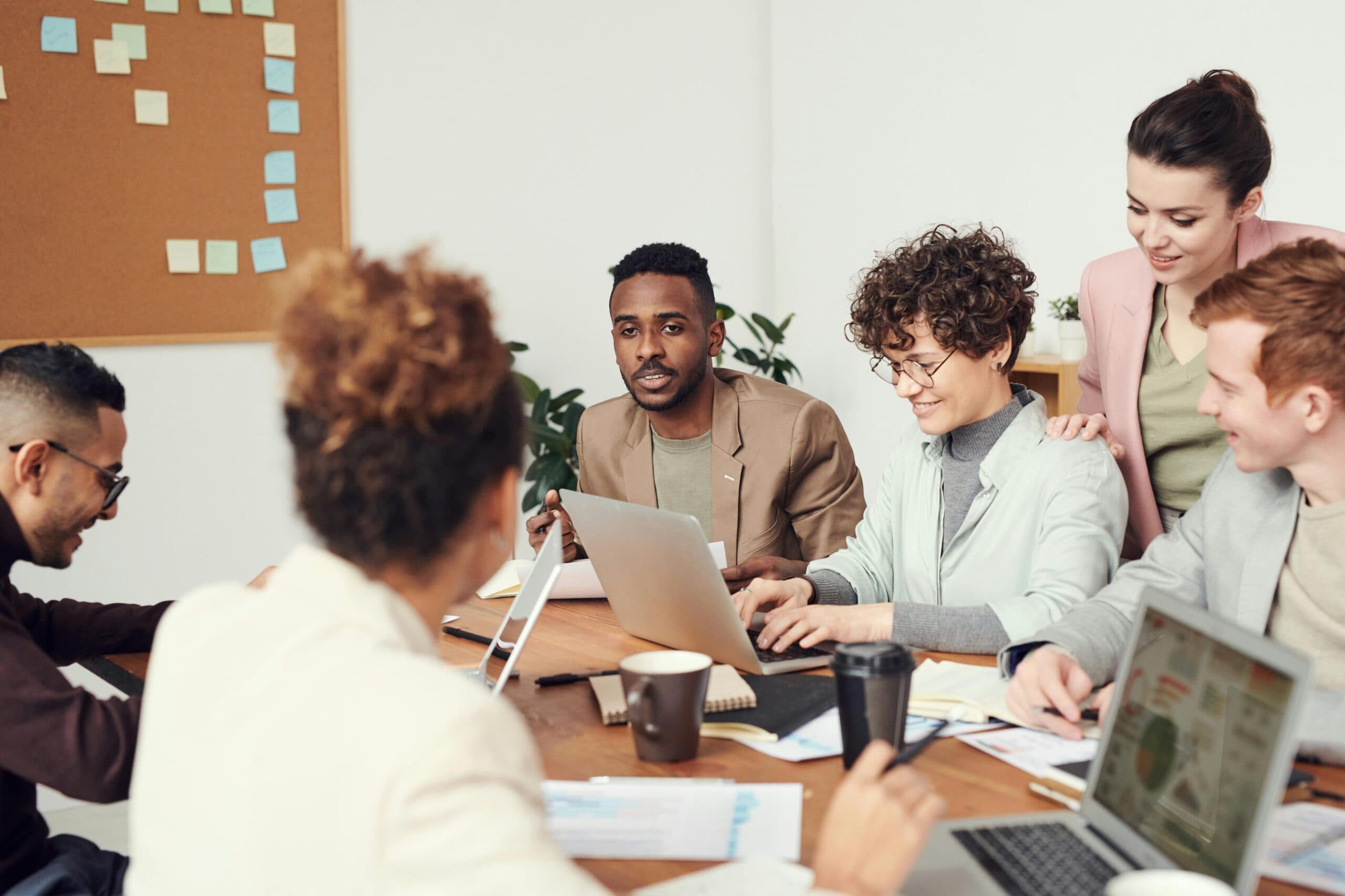 Diverse group of colleagues collaborating around a table with laptops and coffee