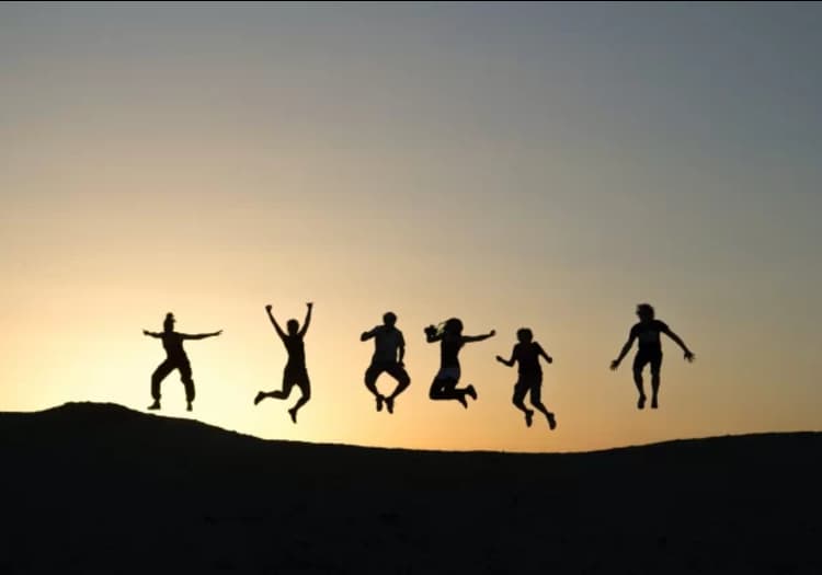 Silhouettes of people jumping for joy against a sunset sky
