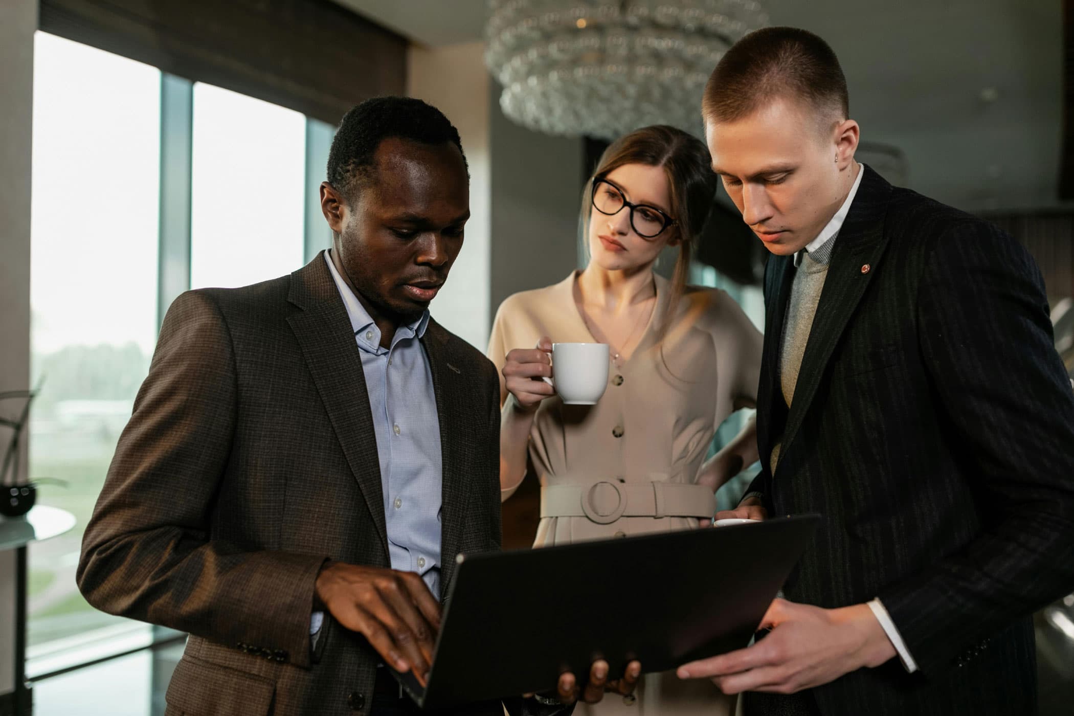 Three professionals in business attire reviewing a laptop together