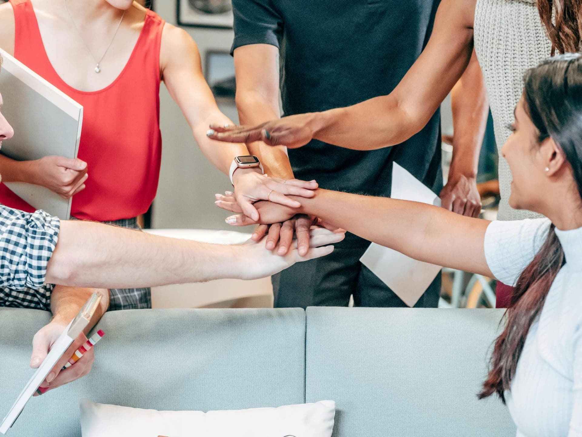 Team members joining hands together over a table covered in charts and devices