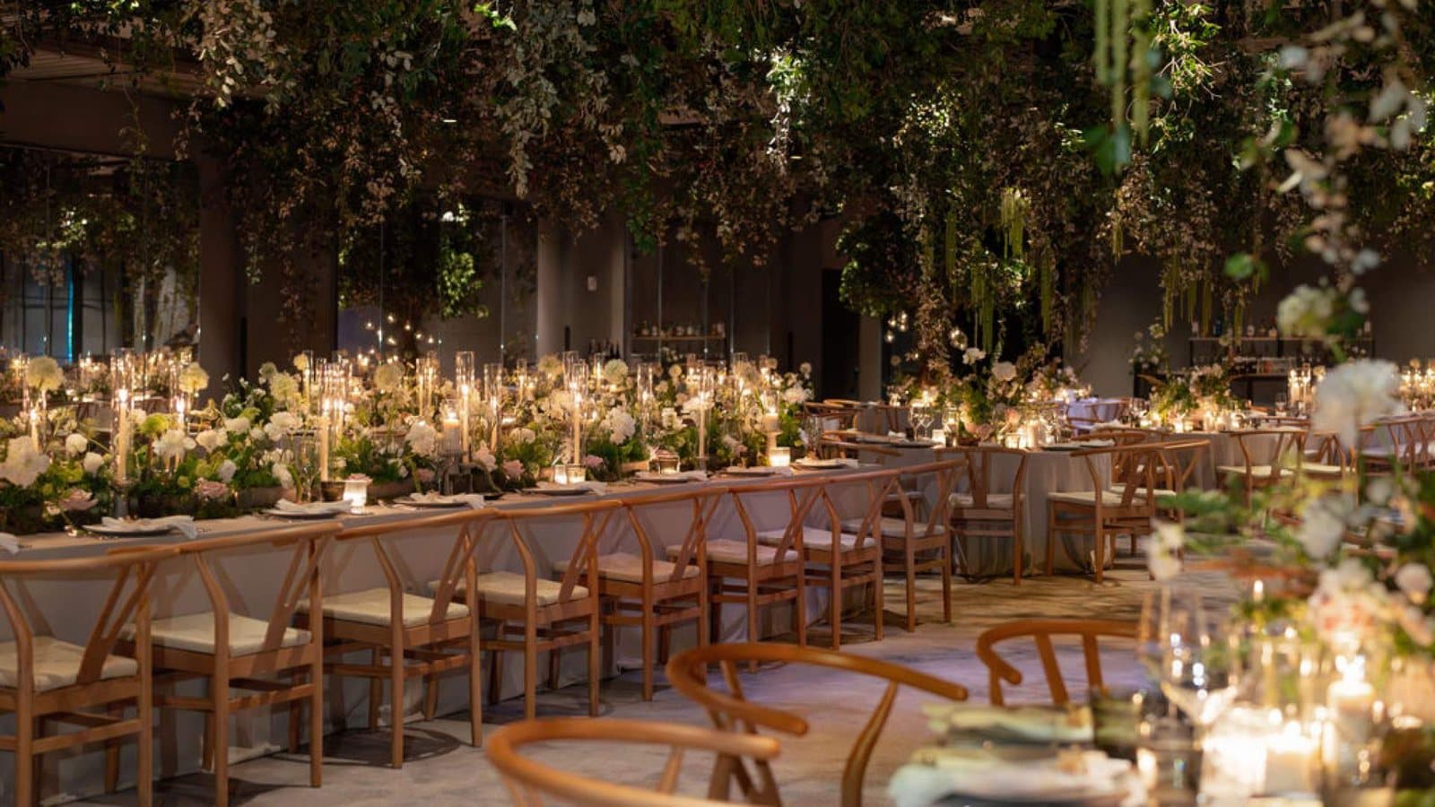 Long dinner tables under hanging greenery and candlelight in an event room at the 1 Hotel Brooklyn Bridge