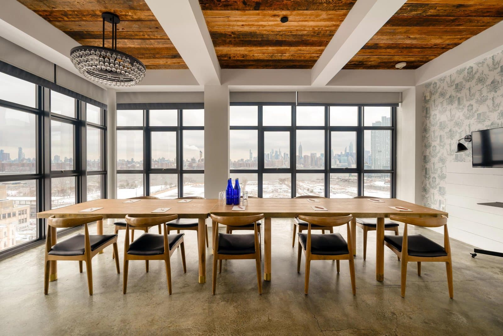 A Wythe Hotel event room with a long table and floor-to-ceiling windows over Williamsburg and Manhattan