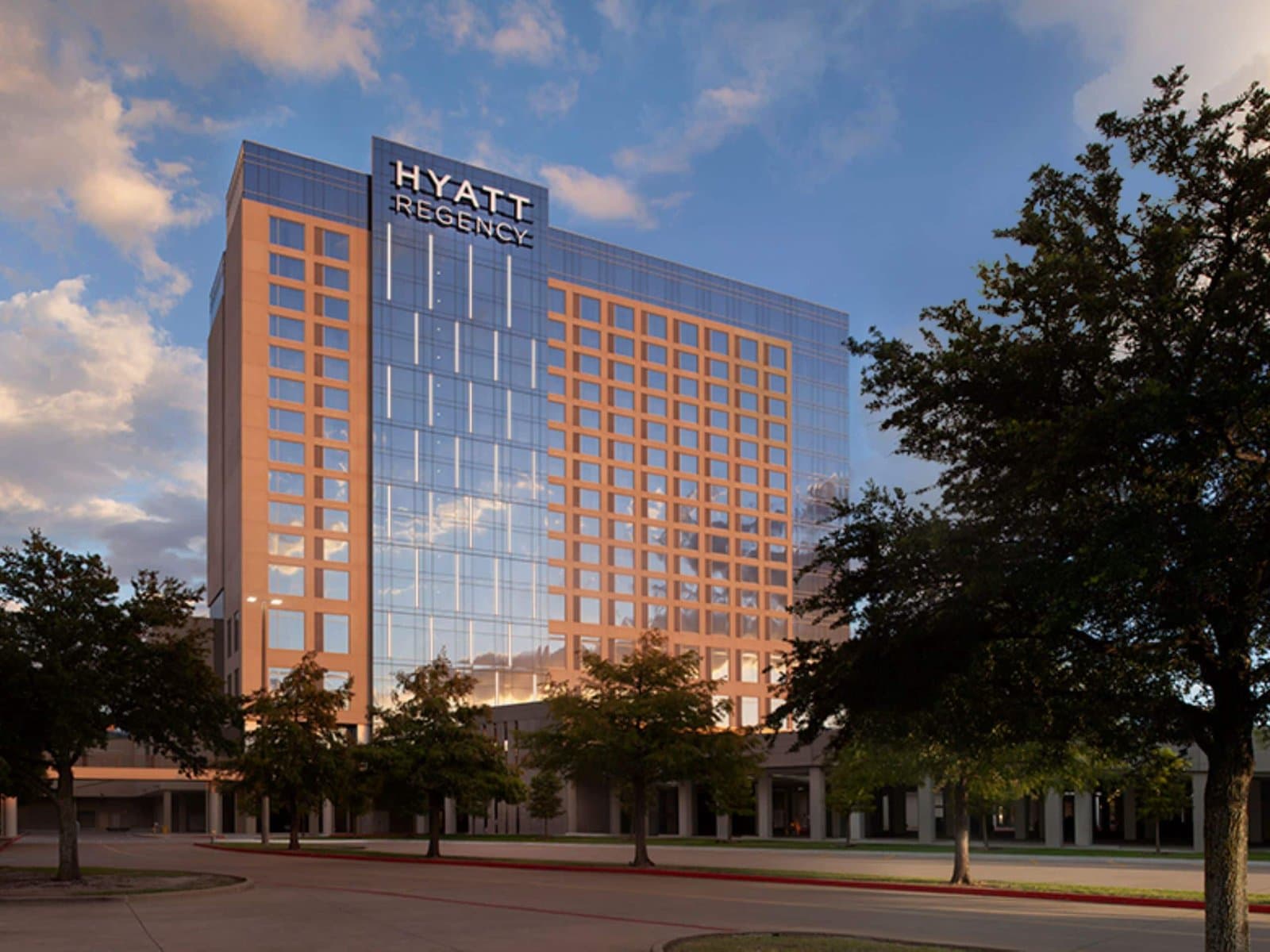 Glass tower of Hyatt Regency Frisco-Dallas in Frisco, Texas, at dusk with oak trees in the foreground