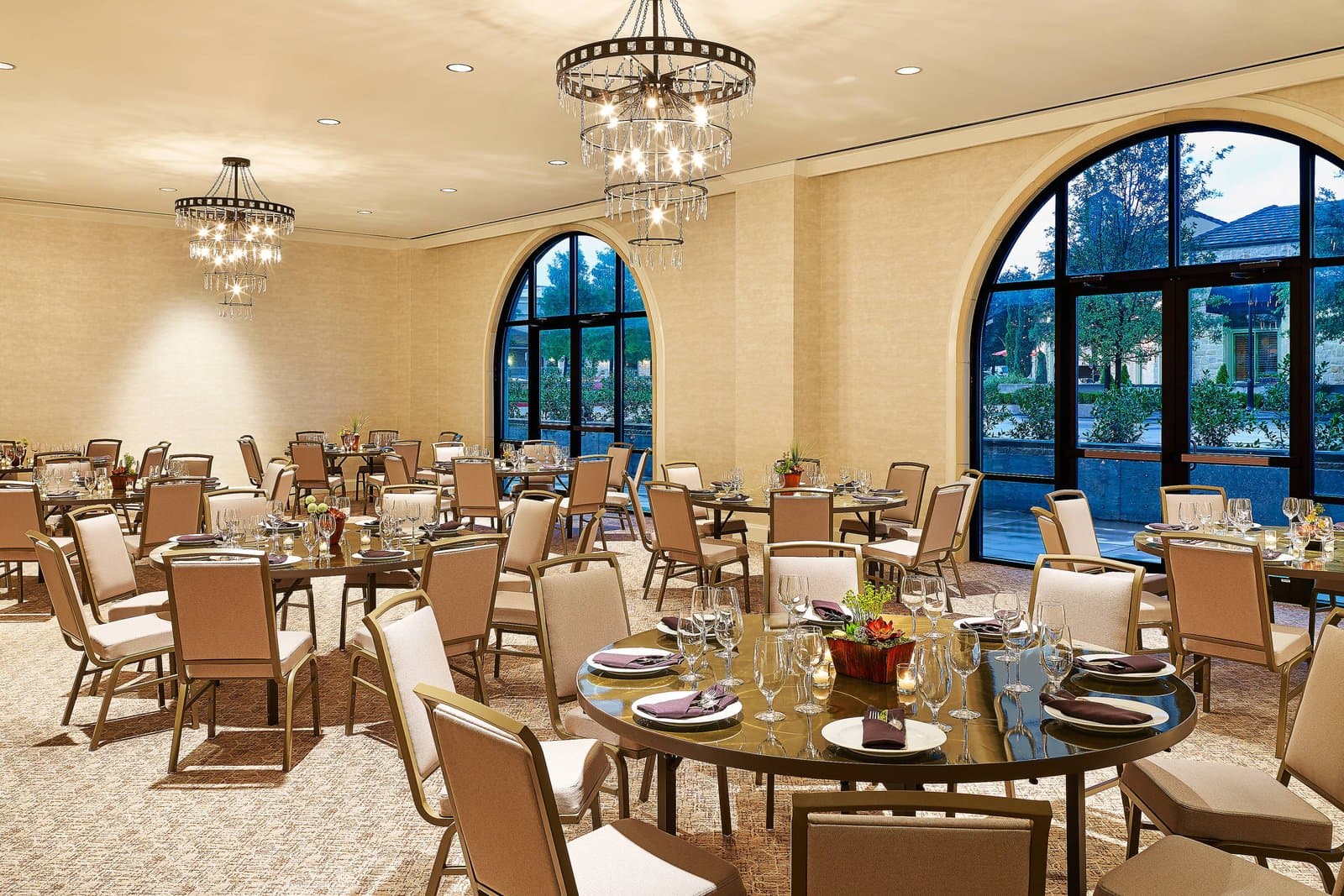 Round banquet tables set under chandeliers and arched windows in the Warren event space at Sheraton Stonebriar Hotel, Frisco