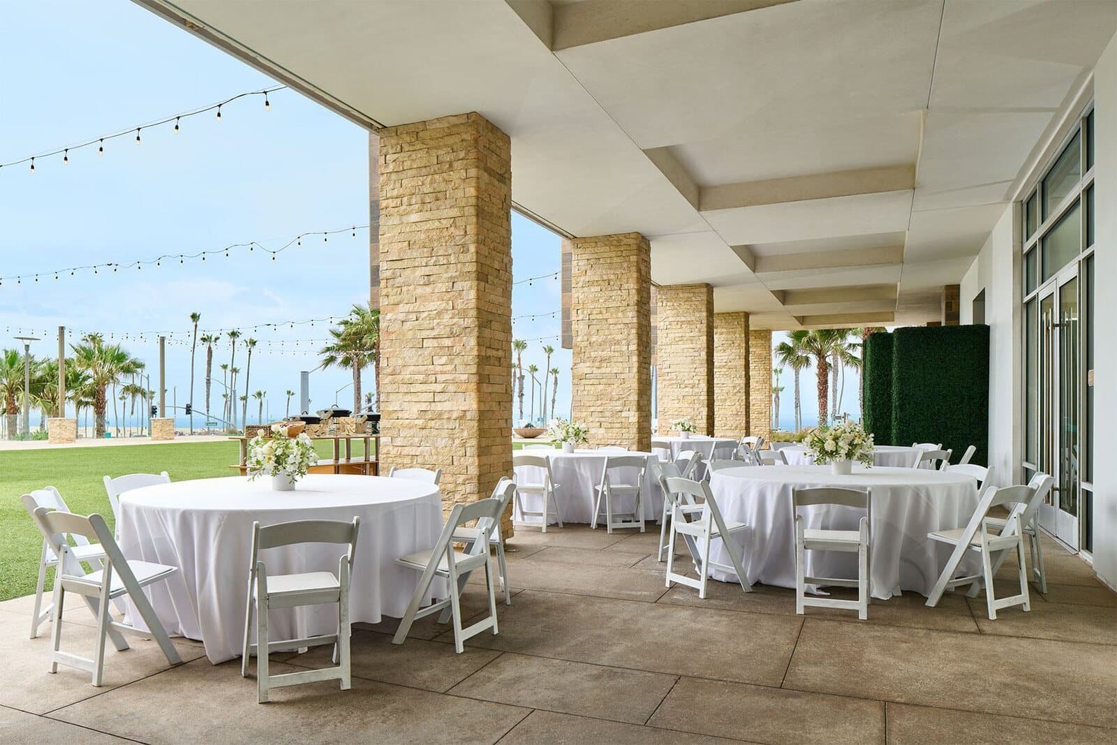 A covered patio at Paséa Hotel & Spa set with round banquet tables beside an oceanfront lawn in Huntington Beach, CA