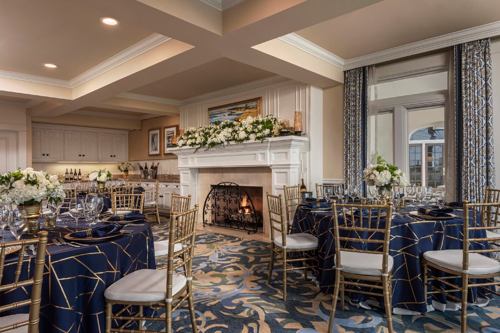 The Sun Room at The Grande Colonial set for a dinner event with a fireplace and navy linens in La Jolla, CA