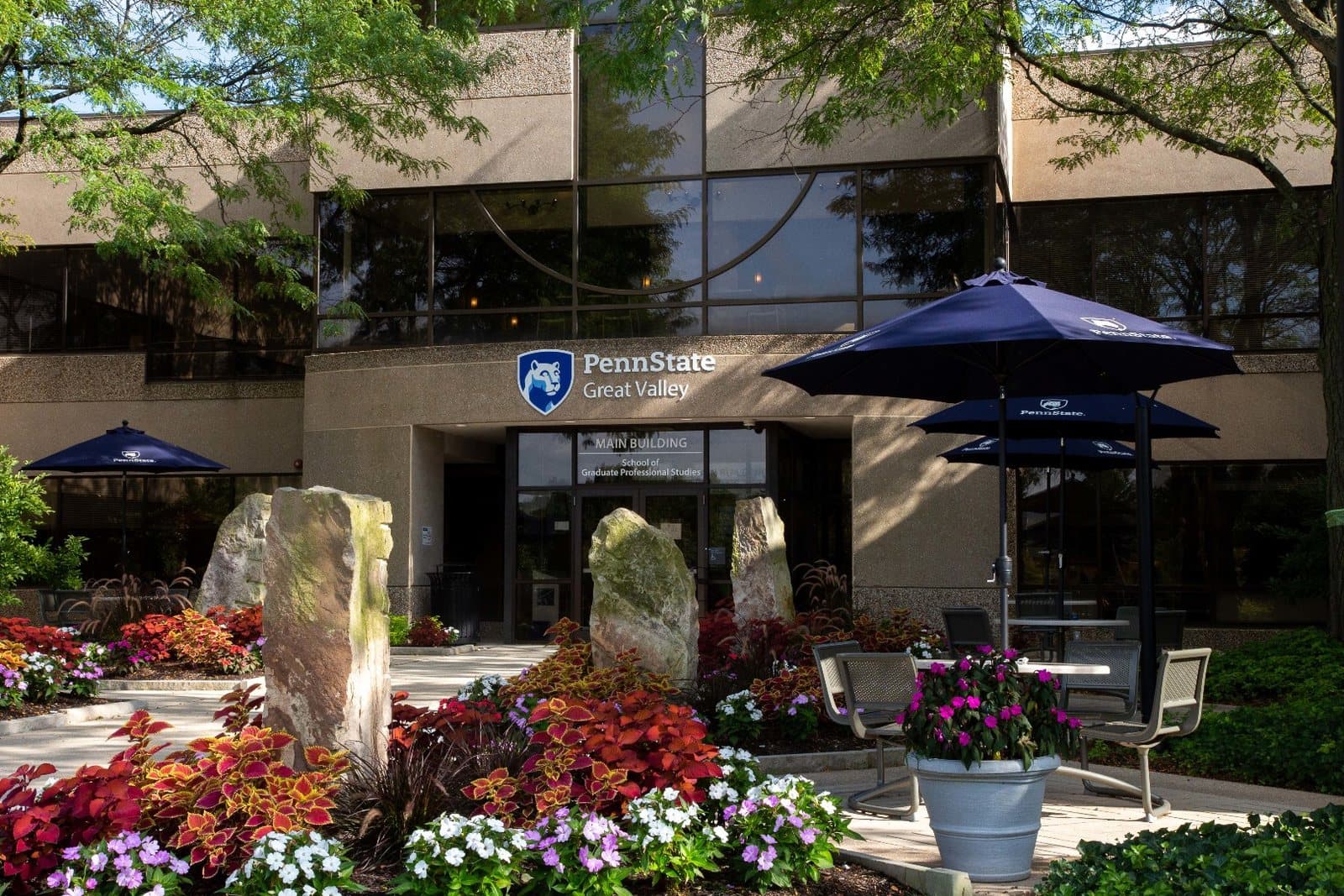 The entrance of Penn State Great Valley's main building behind flower beds and patio umbrellas, Malvern, PA