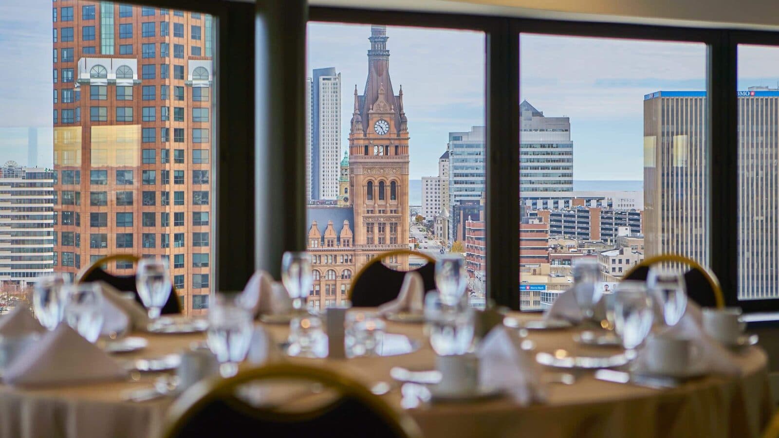 Banquet tables set in the Hyatt Regency Milwaukee's VUE rooftop room, with City Hall's tower through the windows, Milwaukee, WI