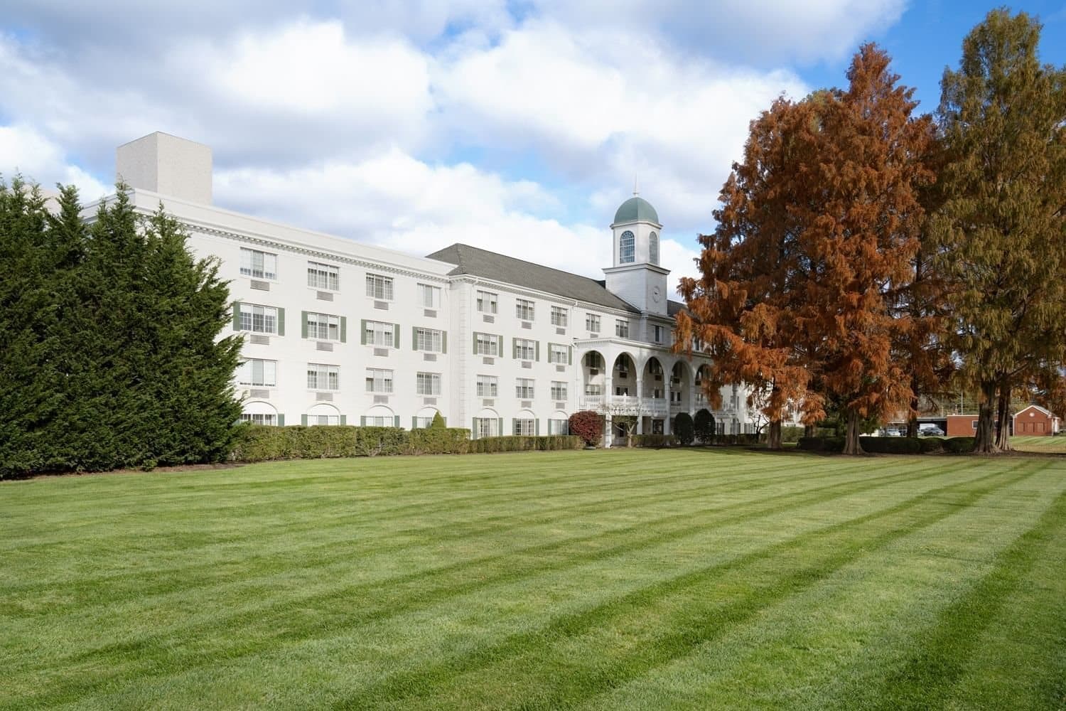 The Madison Hotel's white facade and cupola across a wide lawn in autumn, Morristown, NJ