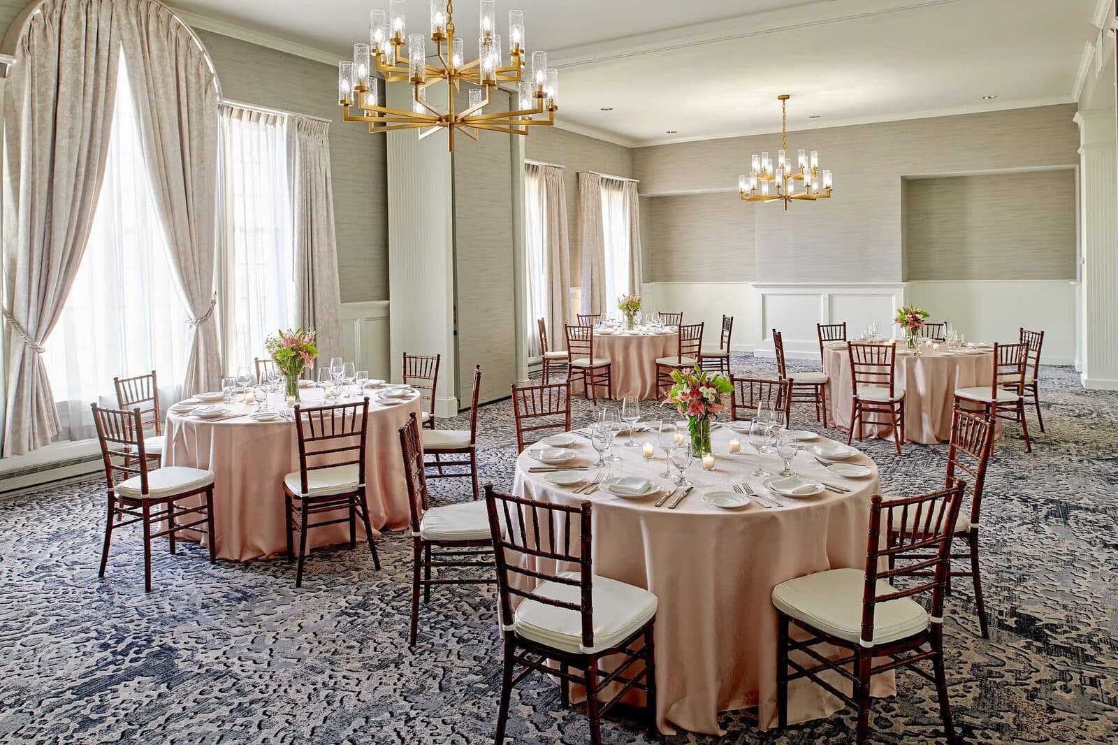 A sunlit event room at Hotel Viking with round tables and brass chandeliers