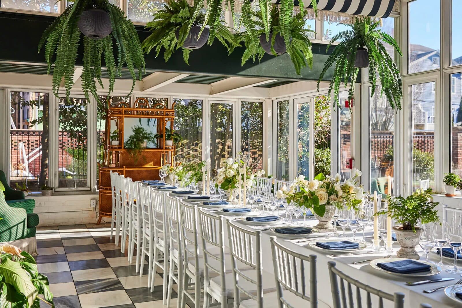 The Vanderbilt's glass conservatory set with a long banquet table under hanging ferns
