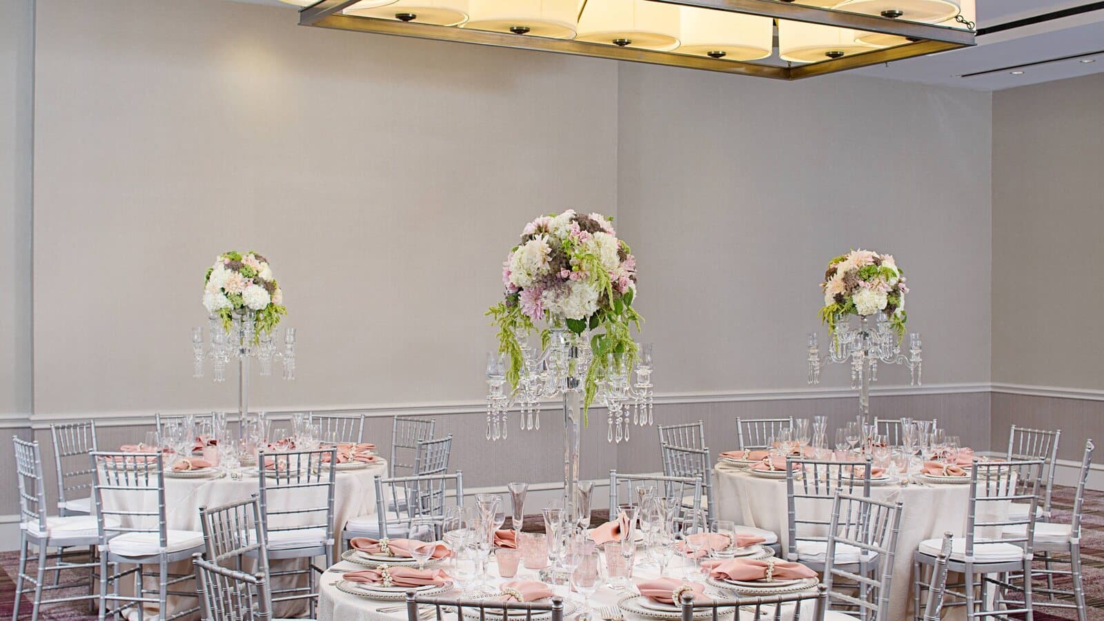 A banquet room at the Pleasanton Marriott in Pleasanton, CA set with round tables, silver chairs and tall floral centerpieces