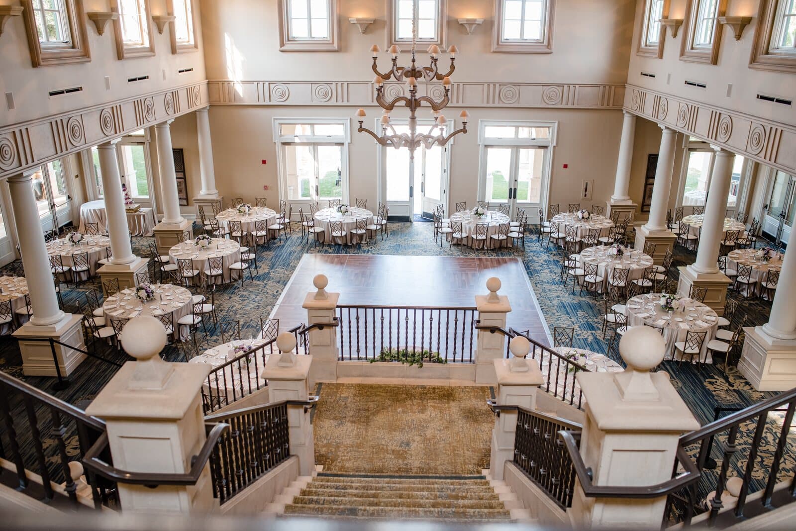 The ballroom at The Club at Ruby Hill in Pleasanton, CA set with round tables, seen from the top of a grand staircase