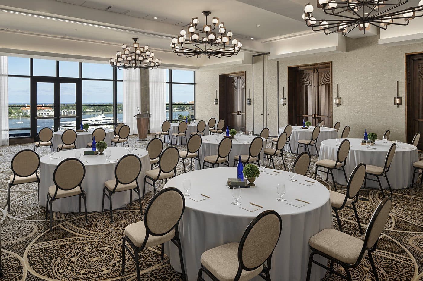 An event room at The Ben set with round tables under chandeliers, windows over the marina, West Palm Beach, FL