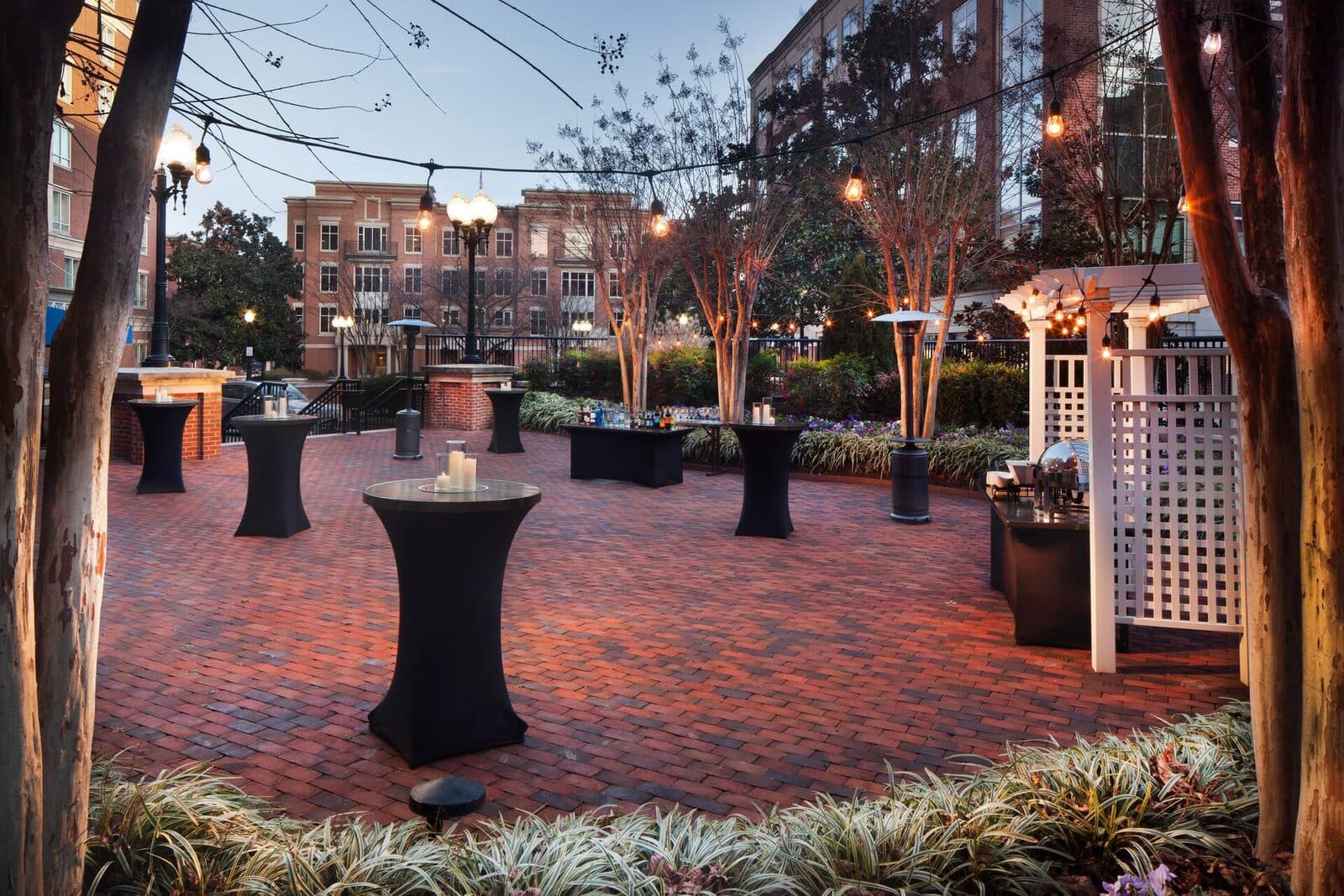 The Hilton Alexandria Old Town brick courtyard set for an evening reception with cocktail tables and string lights, Alexandria, VA