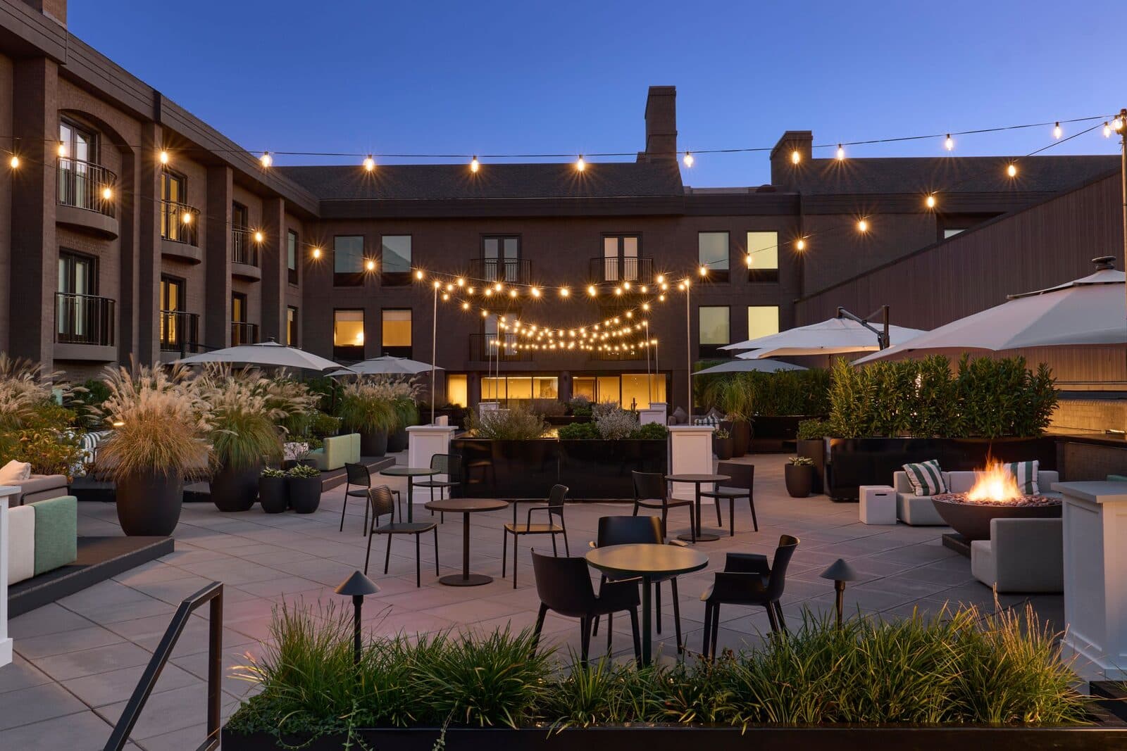 The terrace at The Satire, Autograph Collection at dusk, with fire pits, lounge seating and string lights, Alexandria, VA