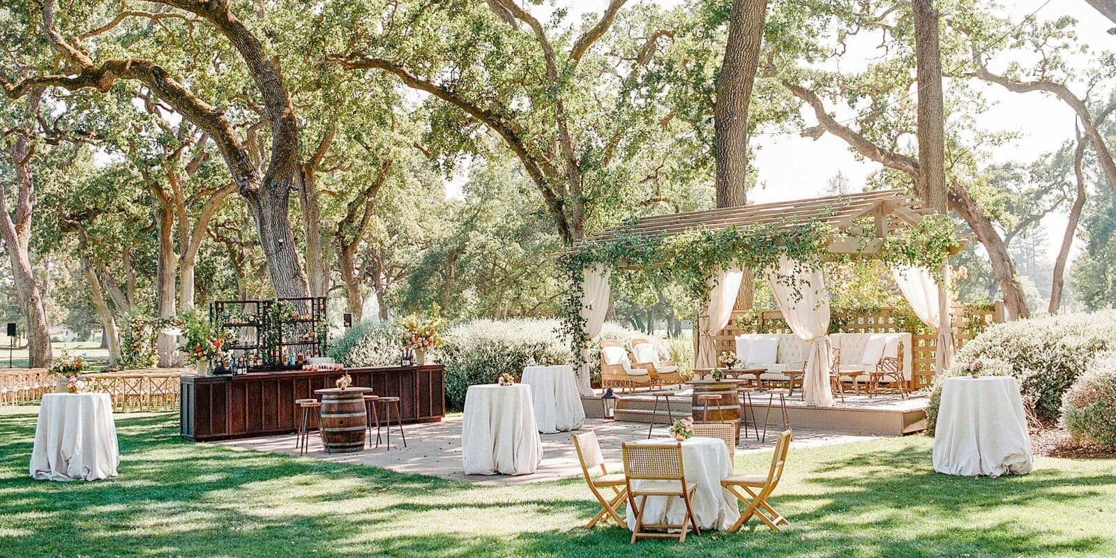 Cocktail tables and a bar set up on the lawn under oak trees at The Grove at Silverado Resort in Napa, CA