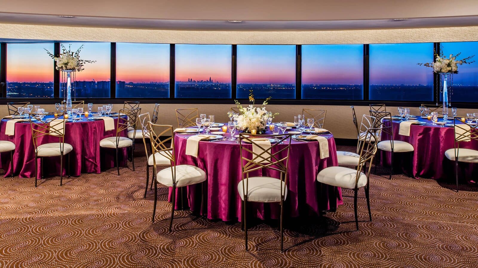 Hyatt Regency O'Hare's Ventanas room set with banquet rounds at sunrise, the Chicago skyline in the windows