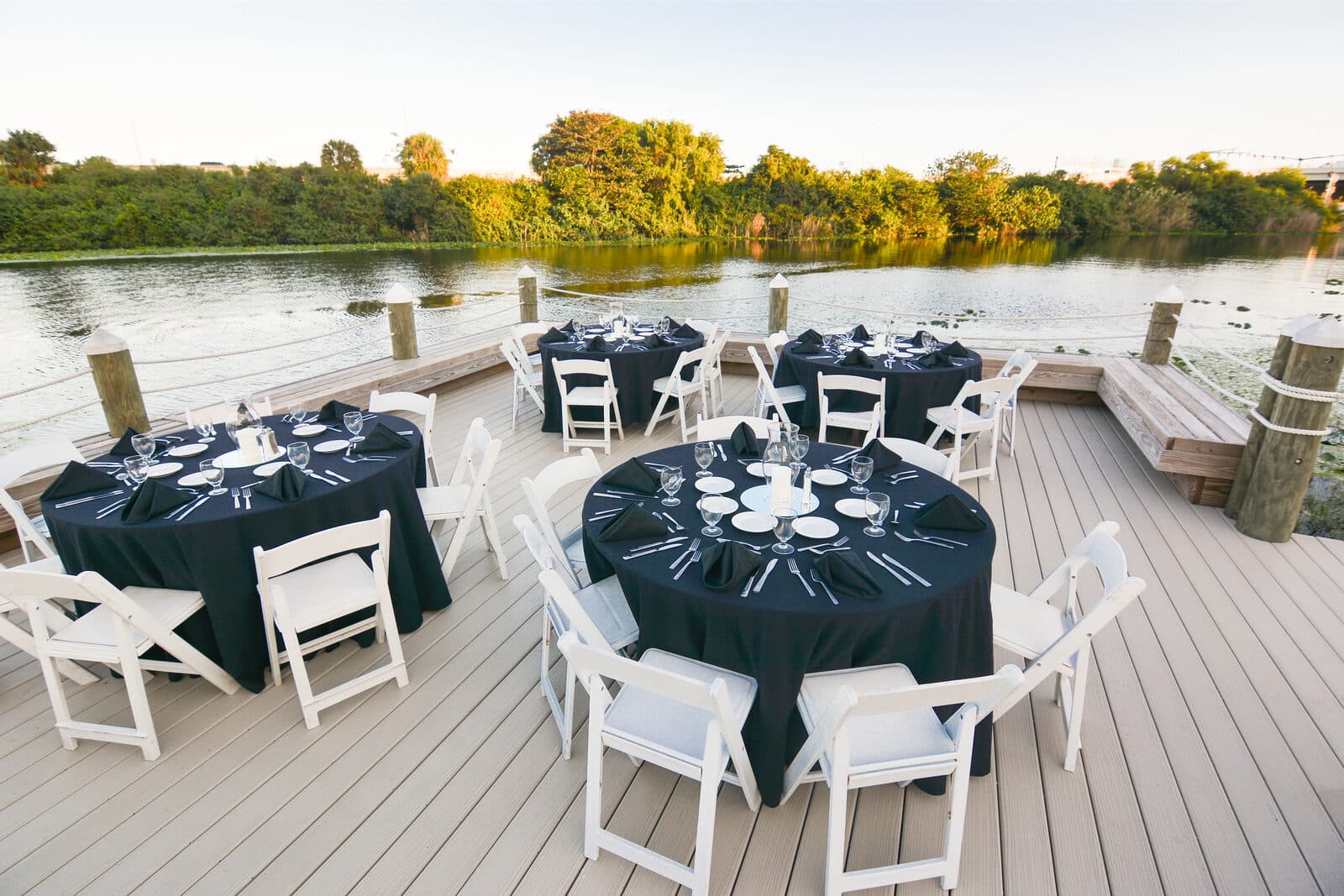 A lakeside deck at the Hilton Palm Beach PBI set with round banquet tables at golden hour