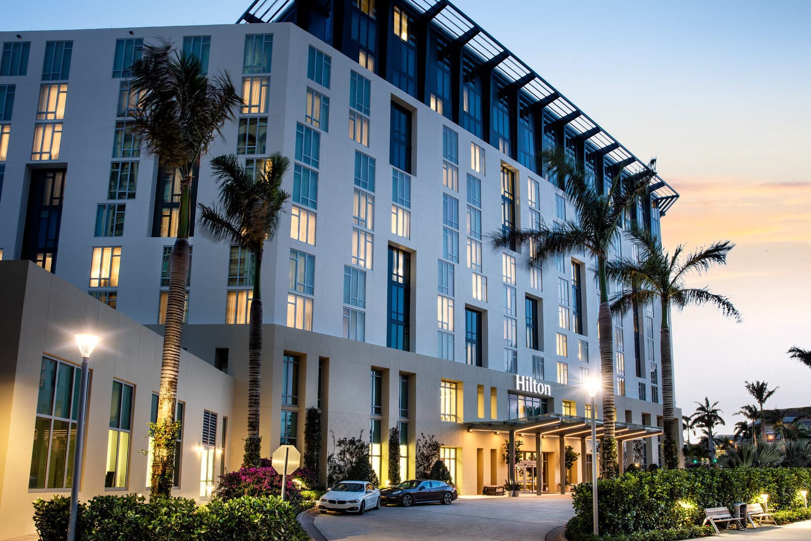 The Hilton West Palm Beach at dusk, with palms along the lit entrance