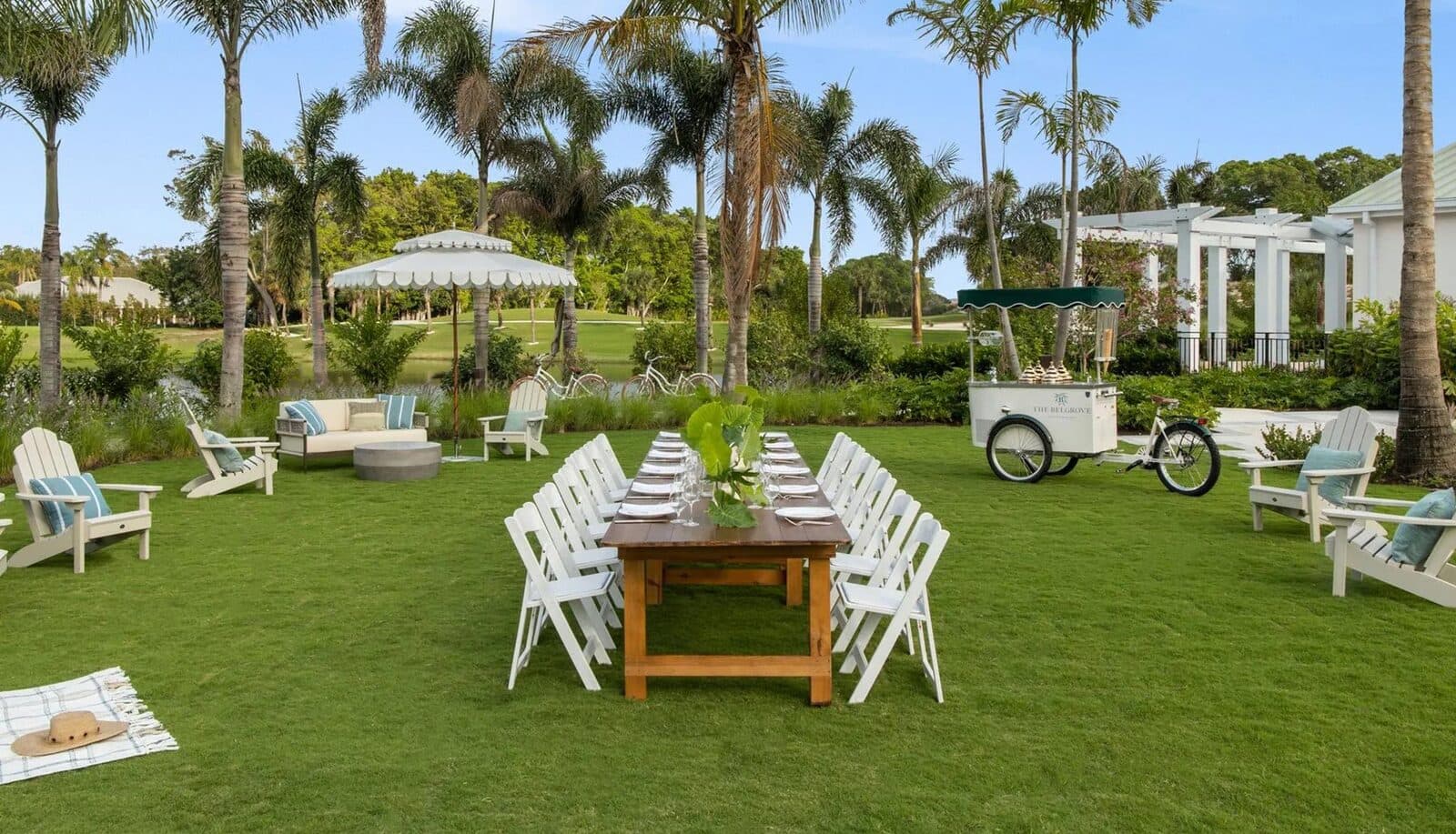 The Belgrove's lakeside lawn set with a long dining table among palms, West Palm Beach, FL