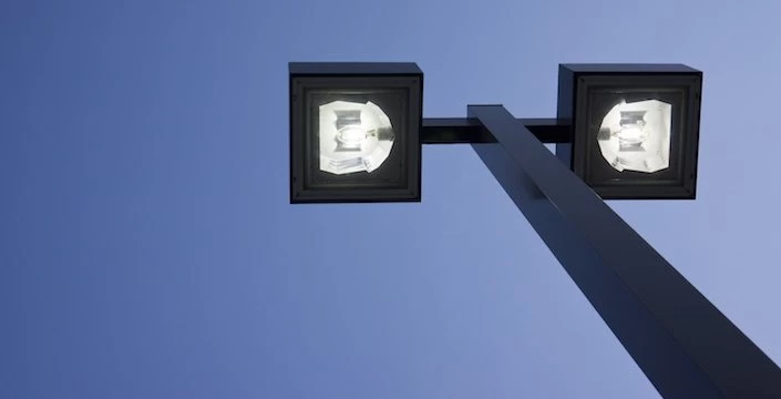 Two street lights against a blue sky.