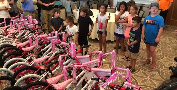 A group of children are standing in front of a room full of bicycles.