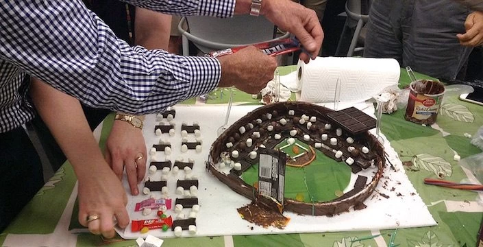 A group of people cutting a cake with a baseball field on it.