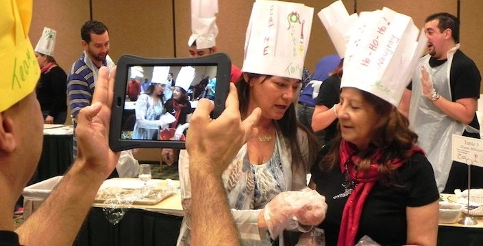 A woman takes a picture of a group of people wearing chef hats.