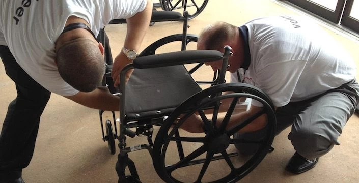 Two men working on a wheelchair in a room.