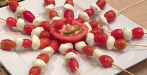 A plate with tomatoes, mozzarella and basil on skewers.