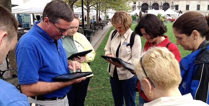 A group of people looking at a tablet in a park.