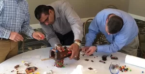 Three men standing around a table making a cake.