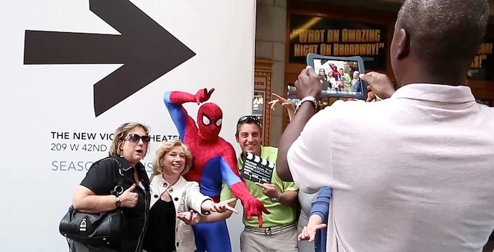 A group of people taking pictures of a spider - man in front of a sign.