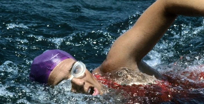 A woman swimming in the ocean with a purple cap and goggles.