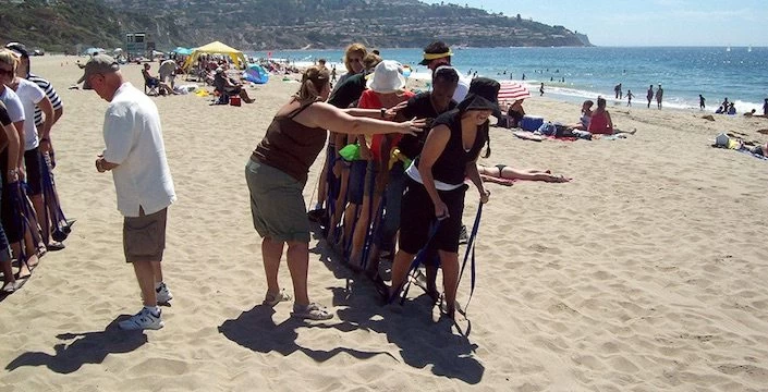 A group of people standing on a beach with a rope.