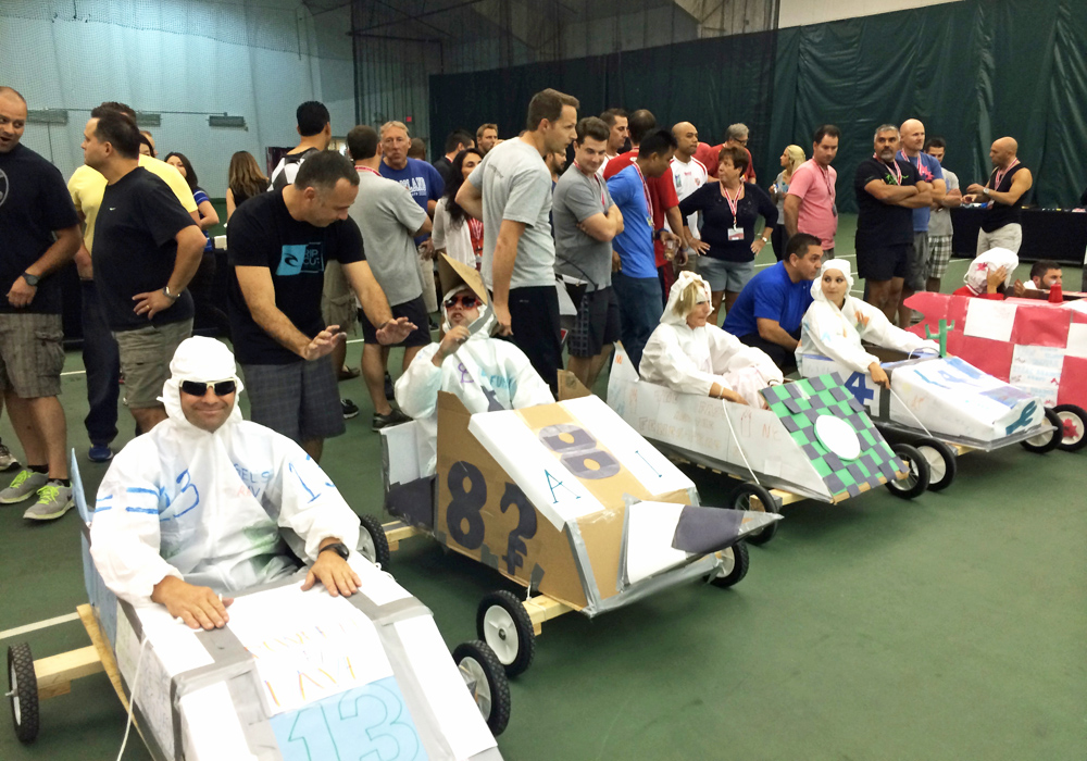 A group of people sitting in cardboard race cars on a court.