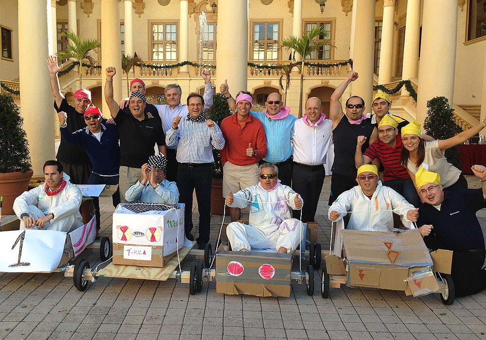 A group of people posing in front of a building with cardboard carts.