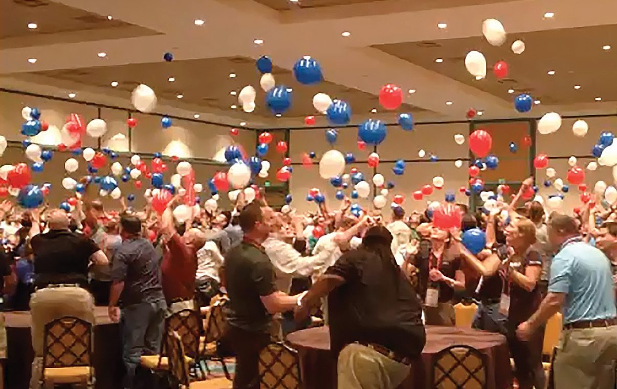 A group of people at a convention with red, white and blue balloons.