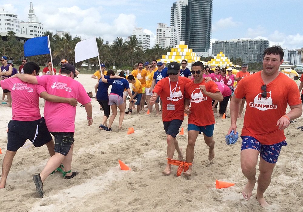 A group of people running on the beach with orange shirts.