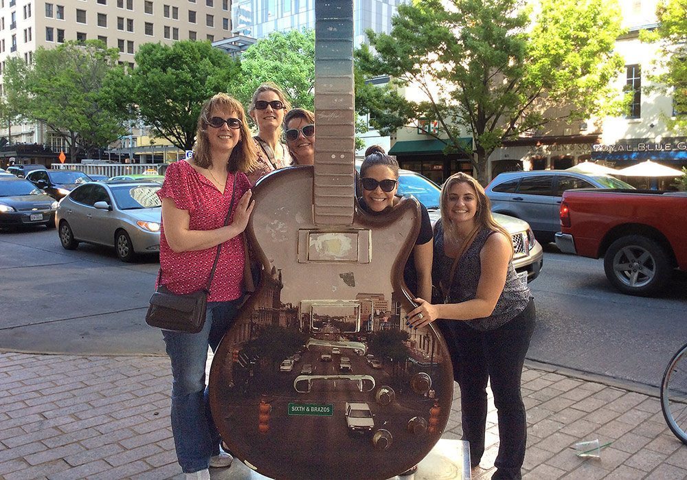 Women posing for a picture with a fake guitar.