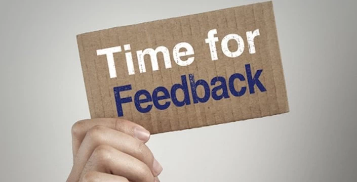 A person holding up a cardboard sign that says time for feedback.