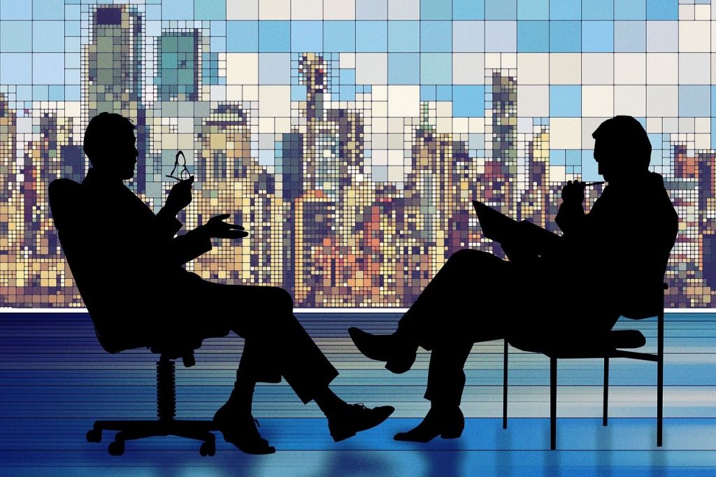 Two silhouettes of business people actively listening to each other in front of a city skyline.