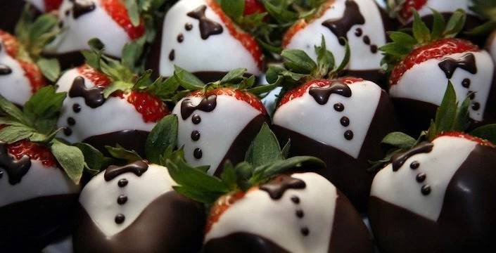 A bunch of chocolate strawberries with tuxedos on them.
