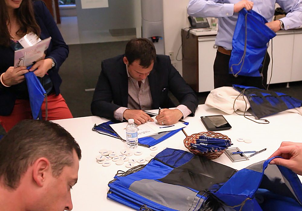 A group of people sitting around a table signing bags.