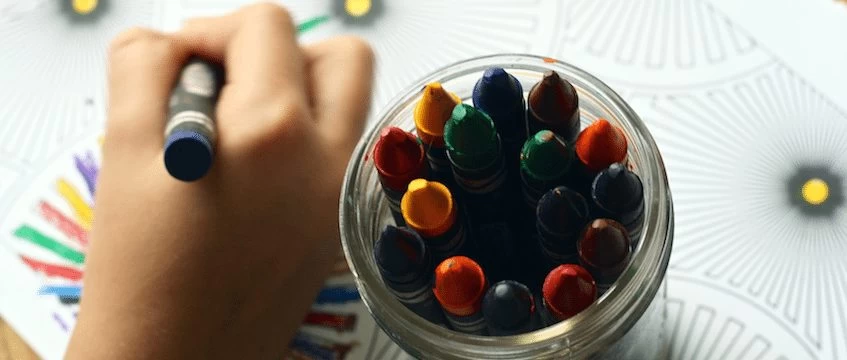 A student is coloring with crayons in a bowl.