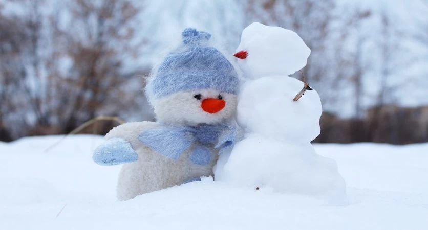 A stuffed snowman is standing next to another snowman in the winter.
